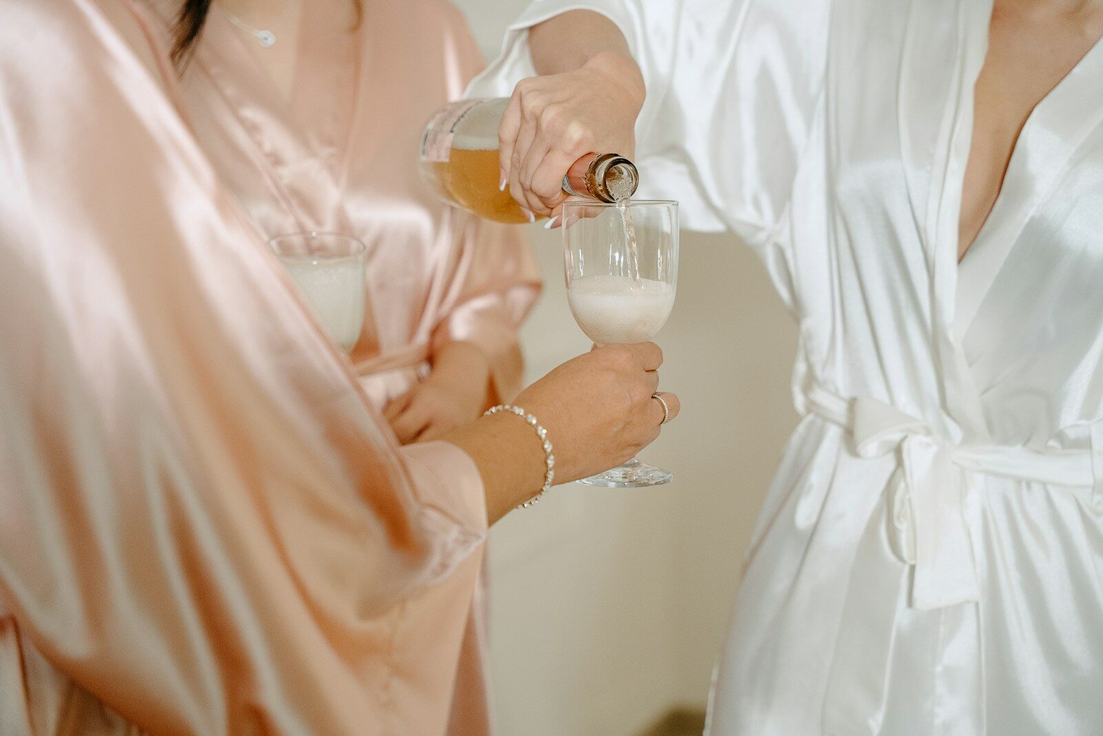 A person in a white robe pouring champagne into a glass for another person.